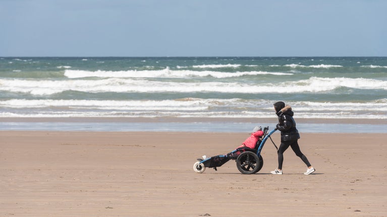 A photograph of a wheelchair user being pushed along Portstewart Strand.